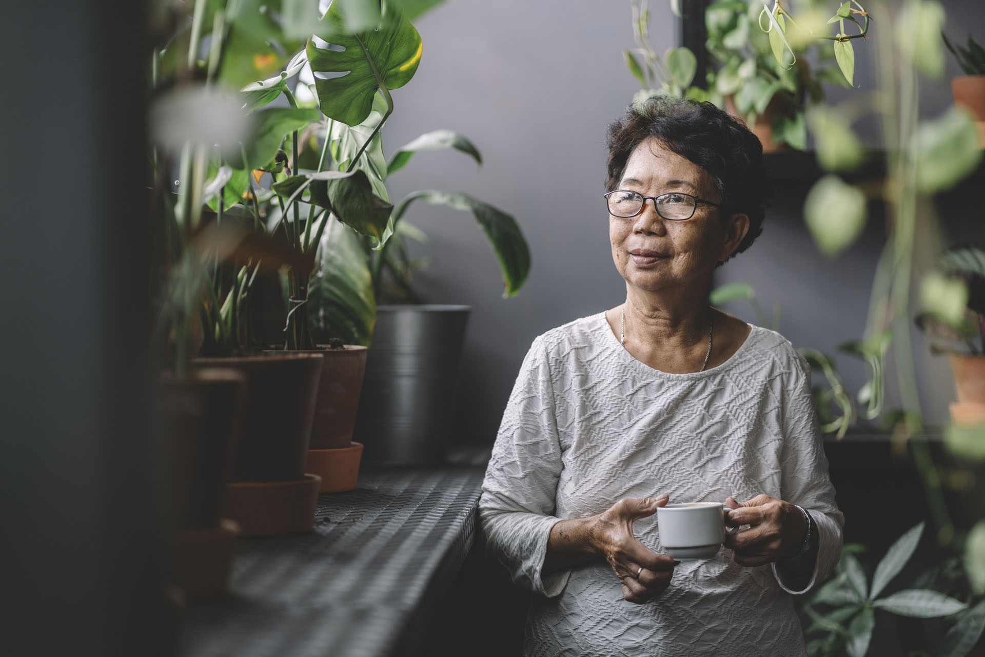Asian woman in room with plants, natural light, holding teacup