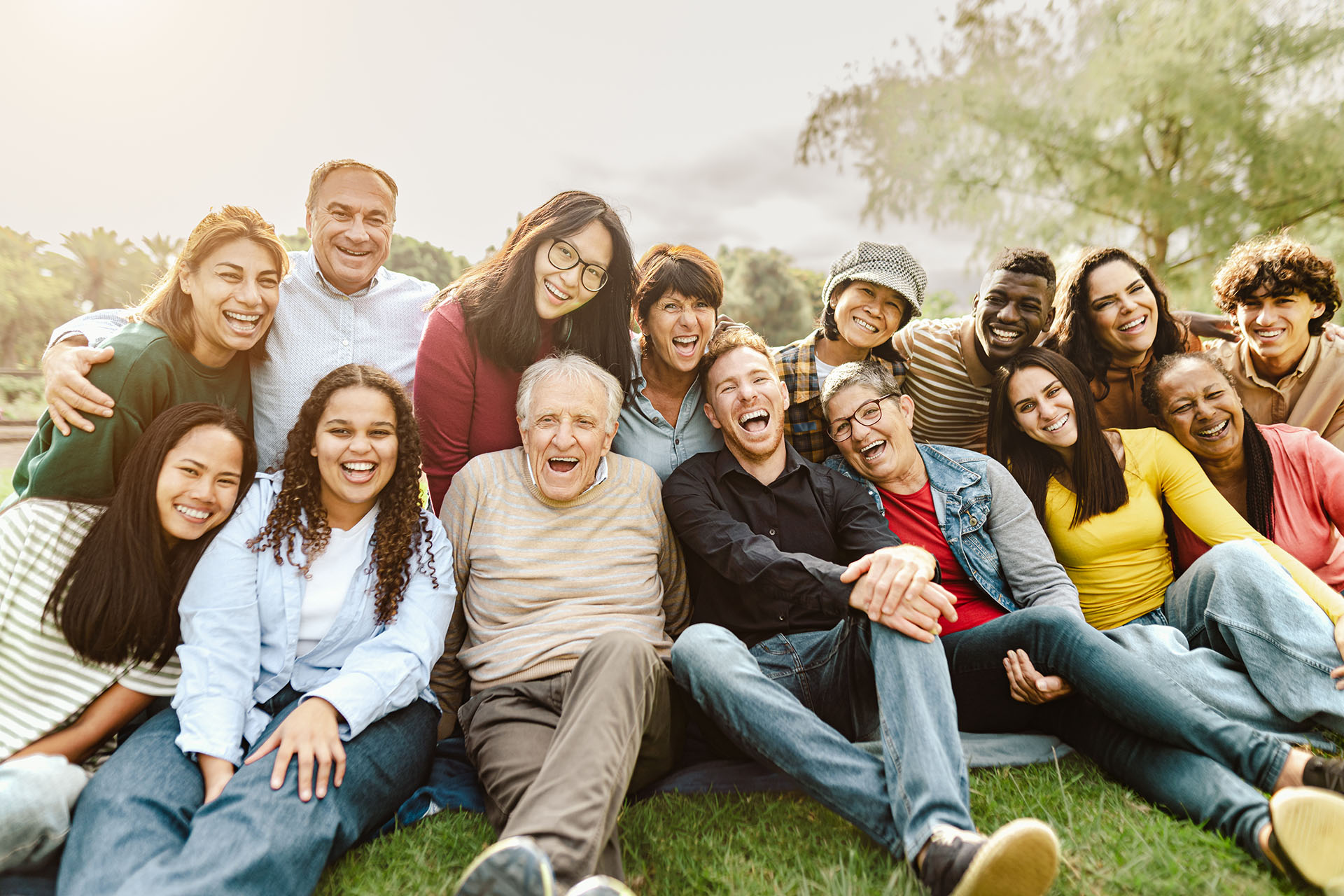 diverse group of people, two rows, similing and sitting on a grassy field outside